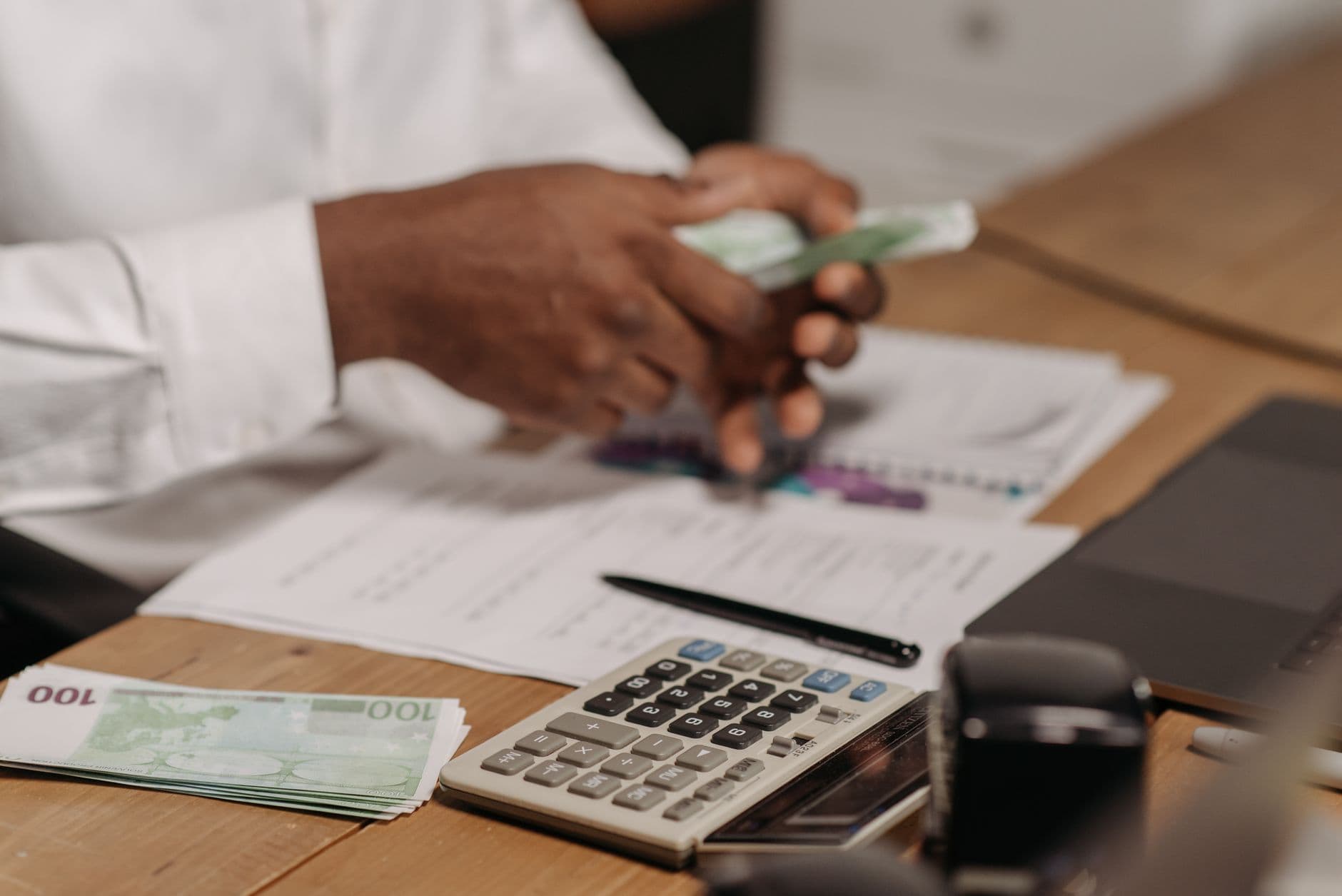 Handen tellen eurobiljetten aan een bureau met rekenmachine en financiële documenten